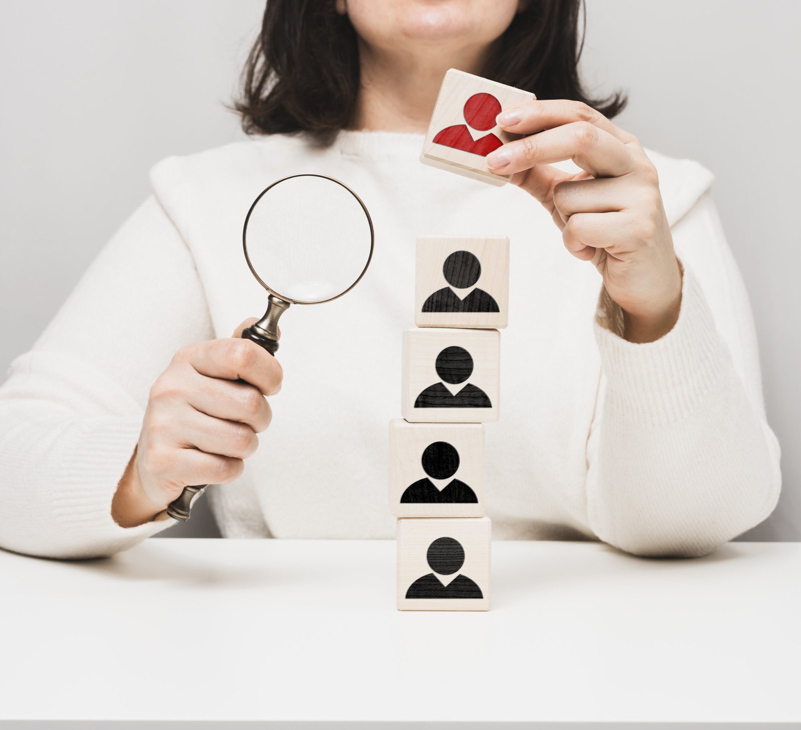 woman holding a magnifying glass and wooden cubes on a white table. Personnel recruitment concept, talented employees. Career advancement